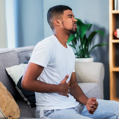 Hombre sentado en el sofá con cara de dolor, tocándose la barriga. / Credit: istockphoto user Emily frost ID:1886551888